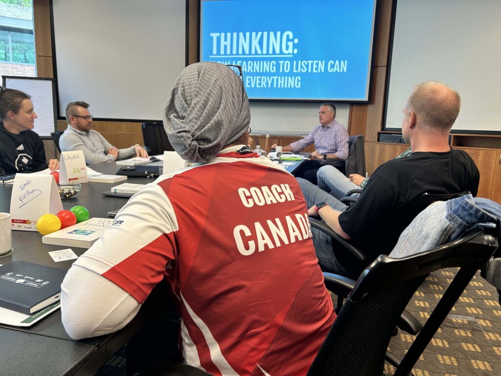 4 people sitting around a table talking with a screen on the wall saying thinking.